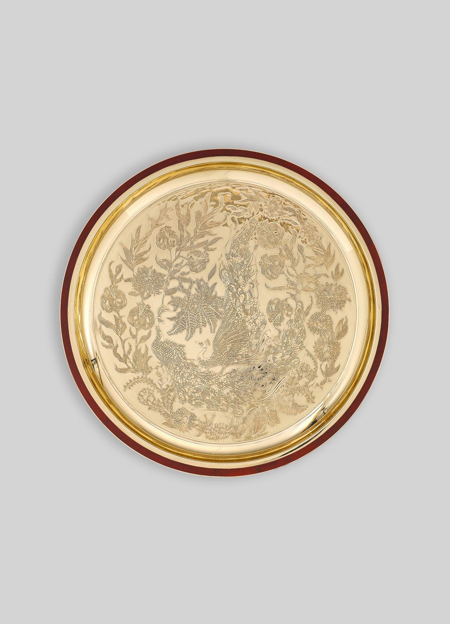 Decorative round tray with engraved floral motifs and a peacock design, made of metal with a gold-toned finish and a dark wood or lacquered border.