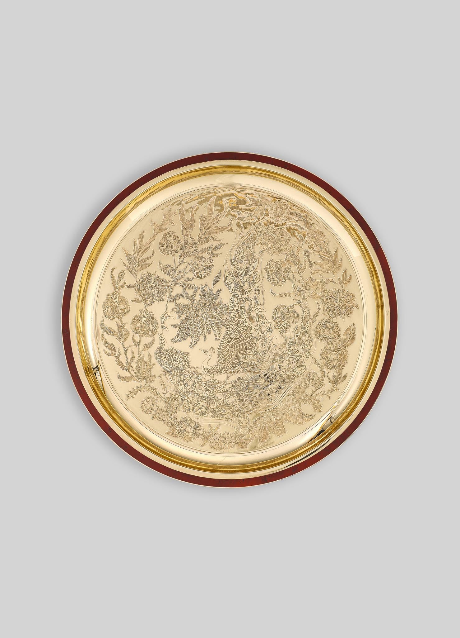 Decorative round tray with engraved floral motifs and a peacock design, made of metal with a gold-toned finish and a dark wood or lacquered border.