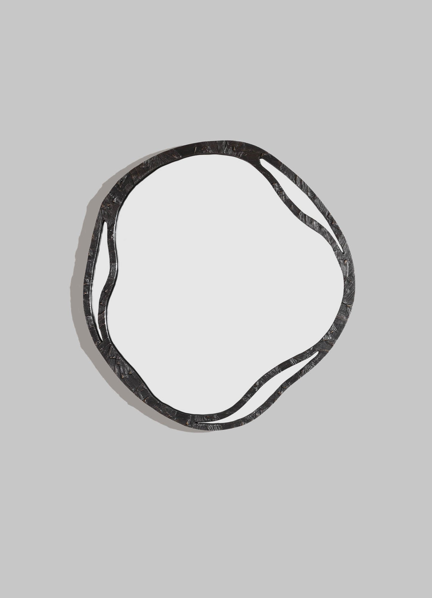 A decorative mirror with an irregular, wavy black metal frame set against a light gray background. The frame features textured, layered metal patterns, creating a modern-rustic style.