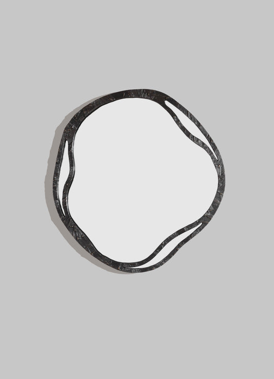 A decorative mirror with an irregular, wavy black metal frame set against a light gray background. The frame features textured, layered metal patterns, creating a modern-rustic style.