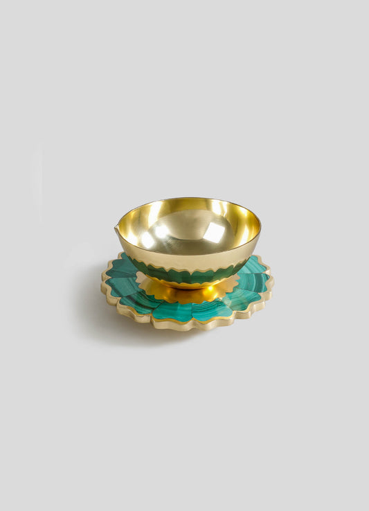 A decorative gold bowl with a reflective interior, placed on top of a turquoise and gold scalloped plate with a floral motif.