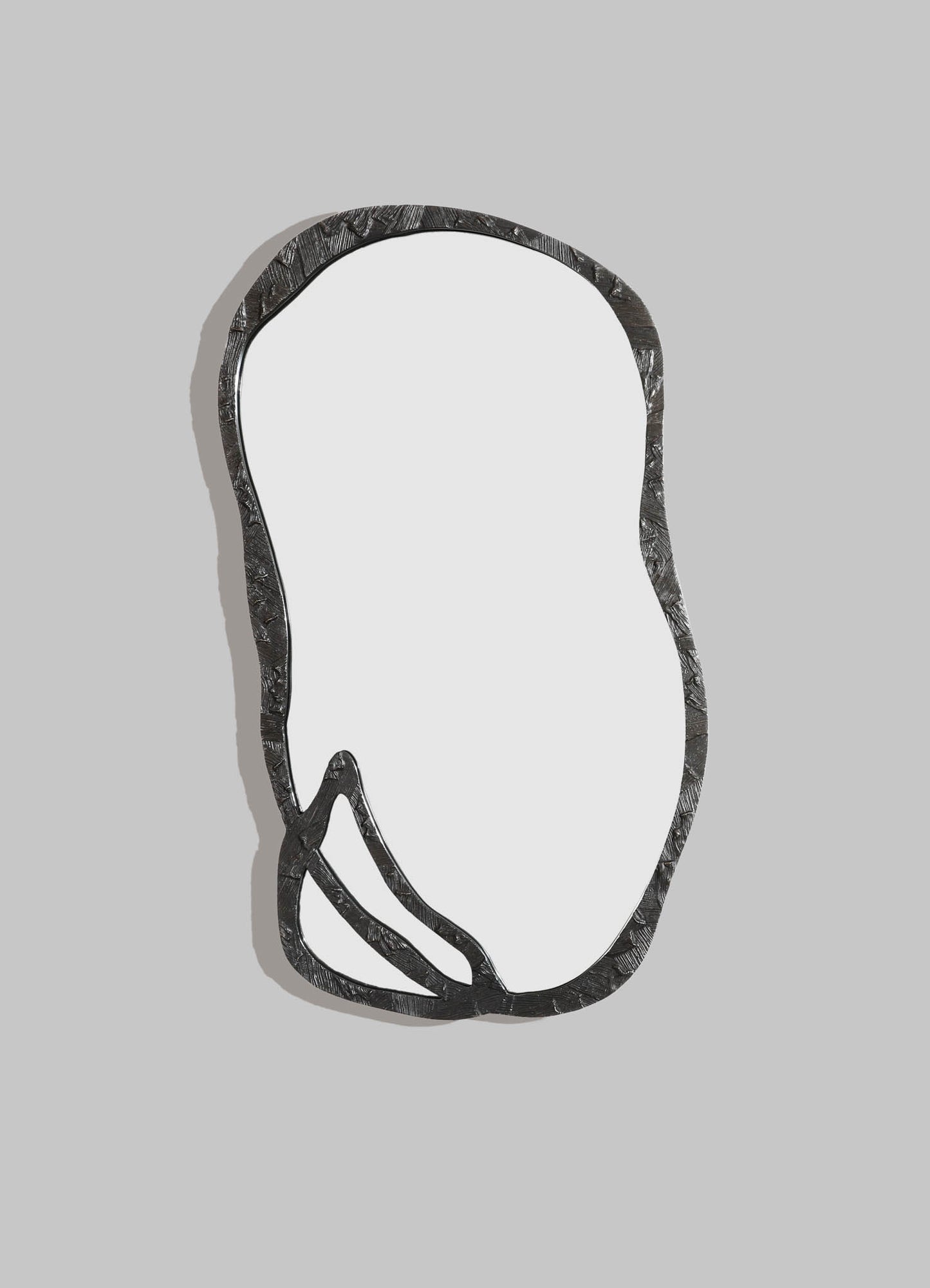 A decorative wall mirror with an irregular, organic-shaped metal frame featuring a textured surface in dark finish, mounted on a light gray background.