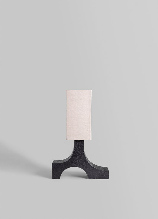 A table lamp with a sculptural black base featuring a textured finish and a rectangular off-white fabric shade, set against a plain light gray background.