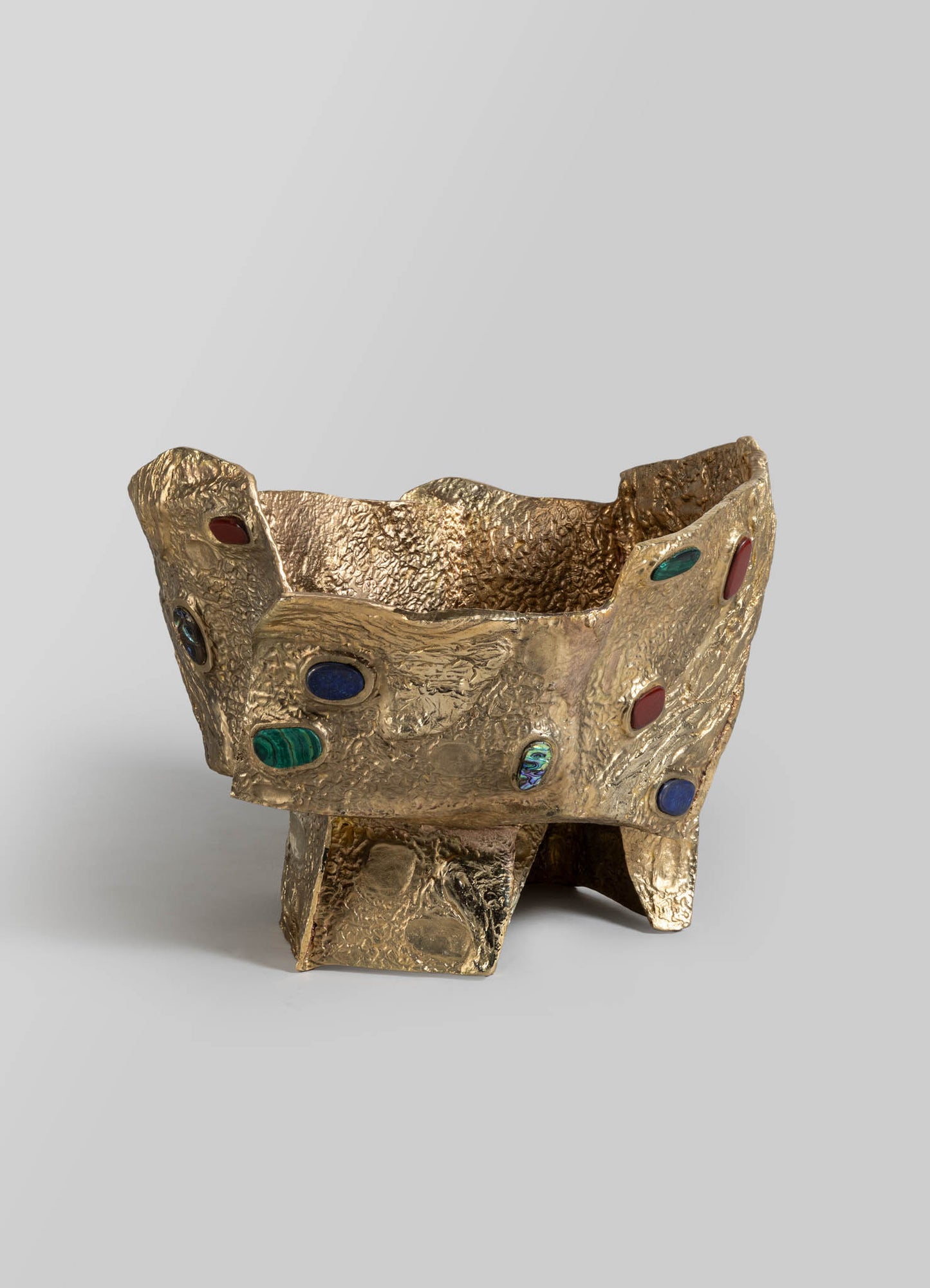 A decorative gold-toned bowl with a textured, irregular surface and embedded colorful stone accents. The bowl features a rugged, handcrafted appearance with a wide opening and a sturdy base.