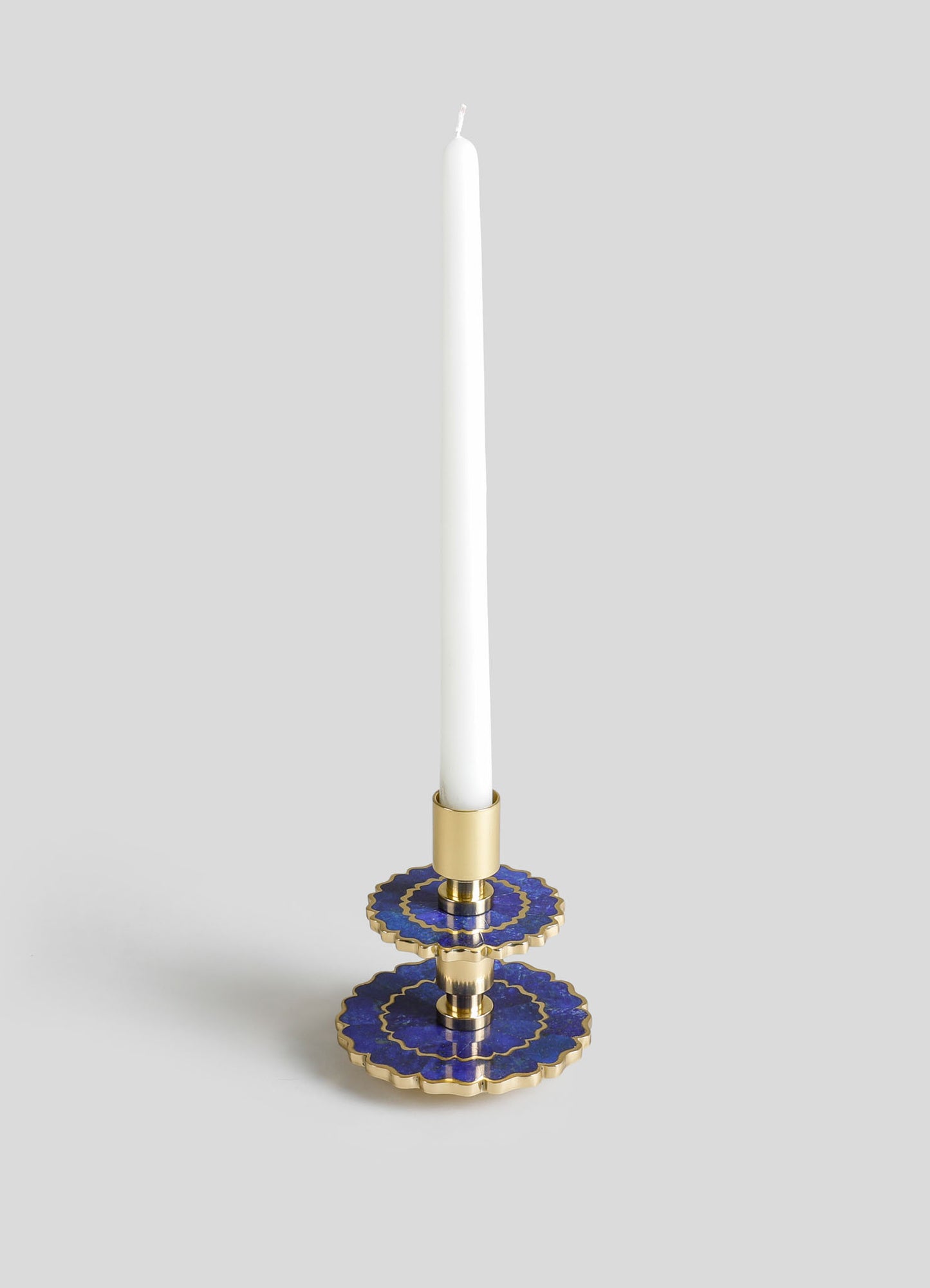 A decorative candle holder with a gold base and scalloped blue ceramic trays featuring gold accents, designed to hold a tall white taper candle.