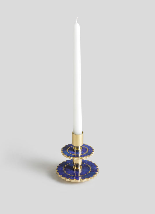 A decorative candle holder with a gold base and scalloped blue ceramic trays featuring gold accents, designed to hold a tall white taper candle.