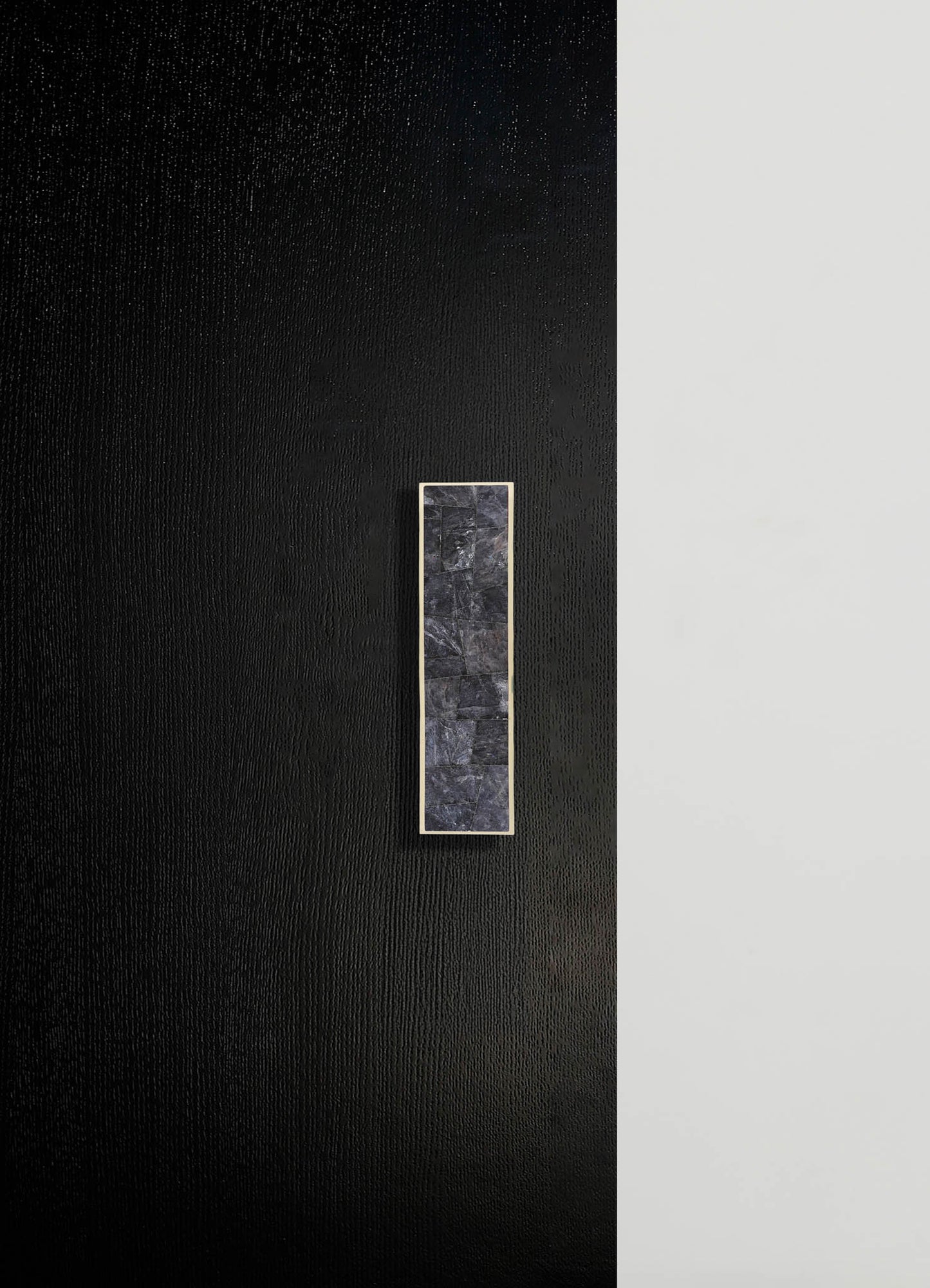 A textured black wall with a narrow vertical marble inlay framed in metal, creating a modern and minimalist design accent.