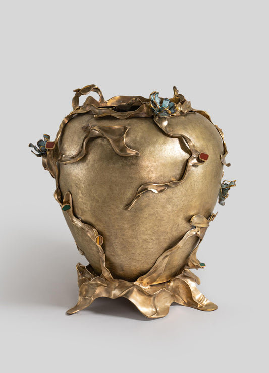 A decorative vases made of metal with a textured gold finish, featuring organic, flowing leaf-like details and accents in jewel tones such as blue, green, and red. The design combines abstract, handcrafted elements with a rustic and luxurious aesthetic.
