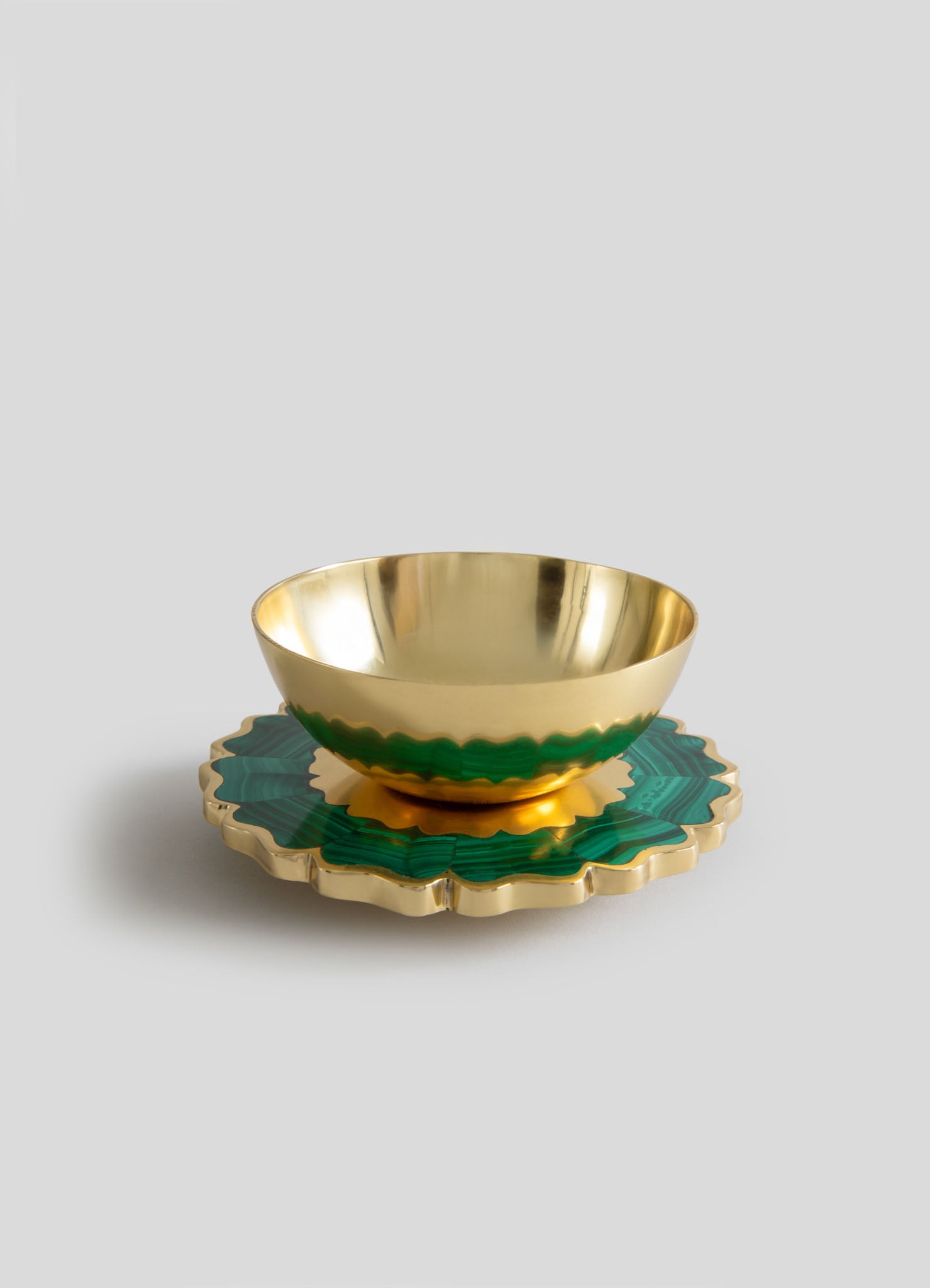 A decorative bowl with a polished gold exterior and a green patterned rim, placed on a matching scalloped-edged tray with gold accents. The set has a luxurious and contemporary style, combining metallic and vibrant colors.