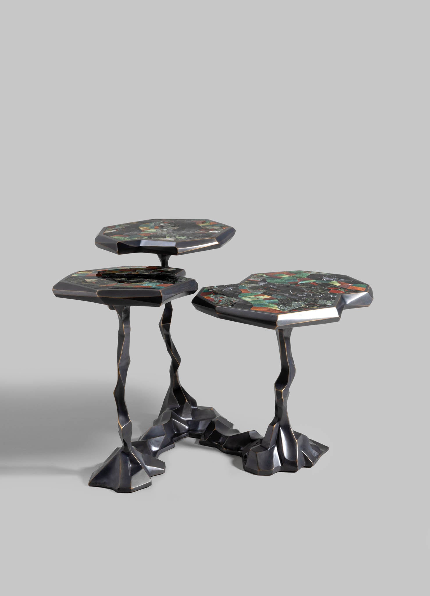 Set of three nesting tables with irregular, sculptural metal legs in a dark finish and multi-colored marble tops featuring a geometric pattern.
