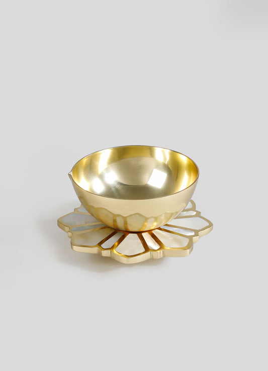 A gold-colored, reflective metal bowl placed on a decorative ceramic coaster with a floral motif and gold accents. The bowl has a smooth, polished surface and a rounded shape, emphasizing an elegant and luxurious style.