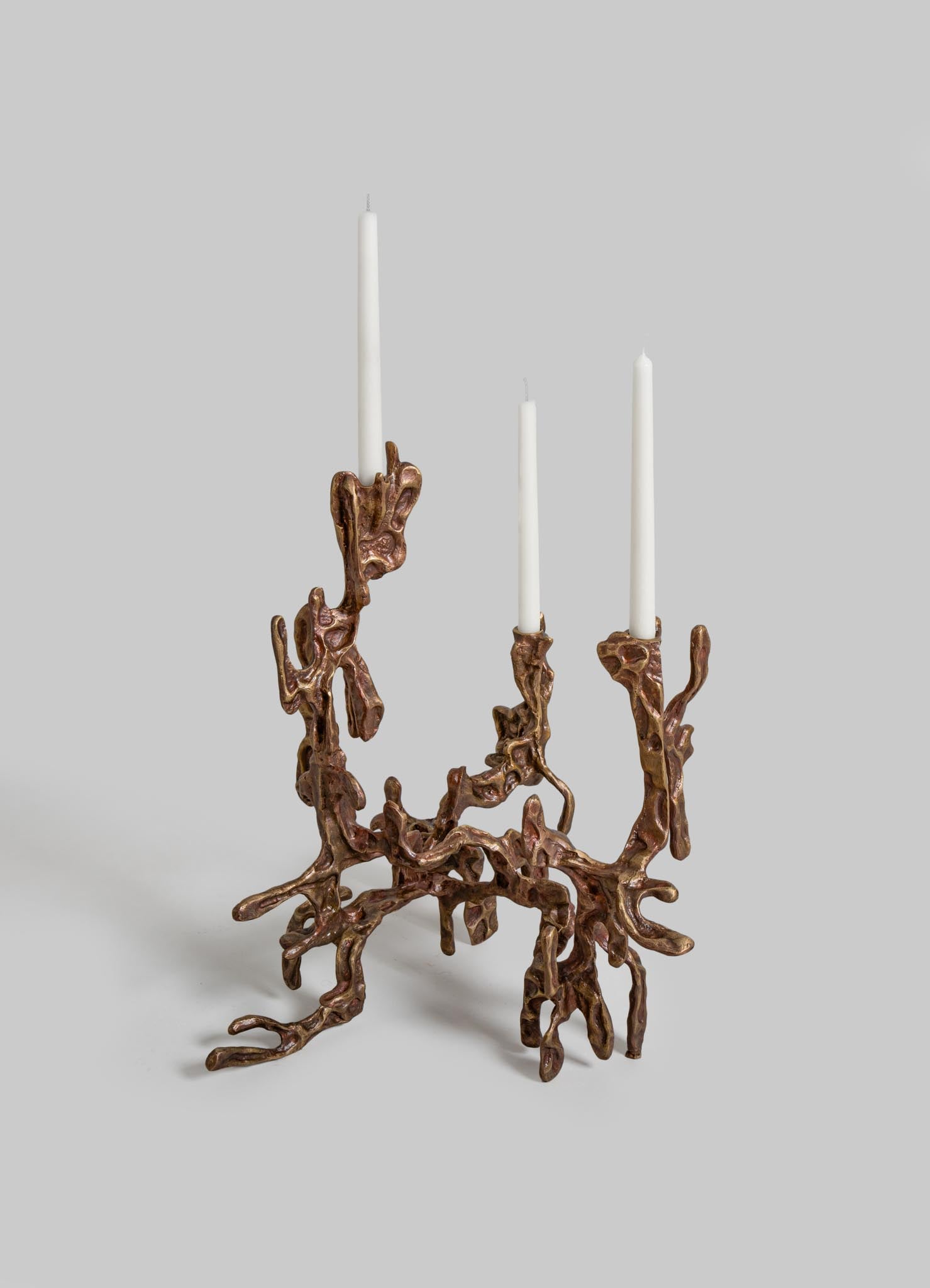 Handcrafted candle holder made of textured bronze metal with an organic, branch-like design, holding three tall white taper candles.
