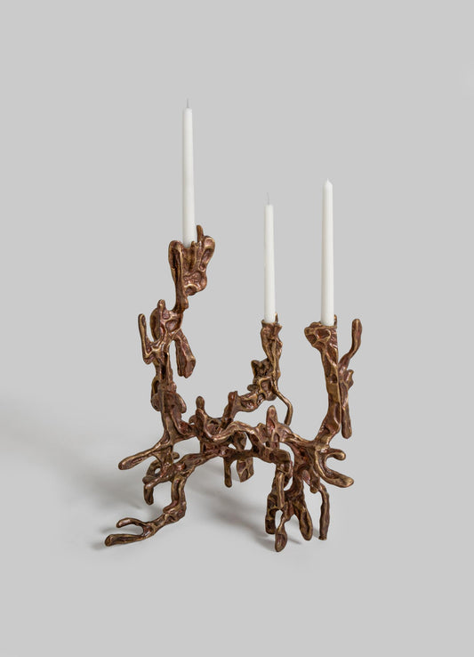 Handcrafted candle holder made of textured bronze metal with an organic, branch-like design, holding three tall white taper candles.