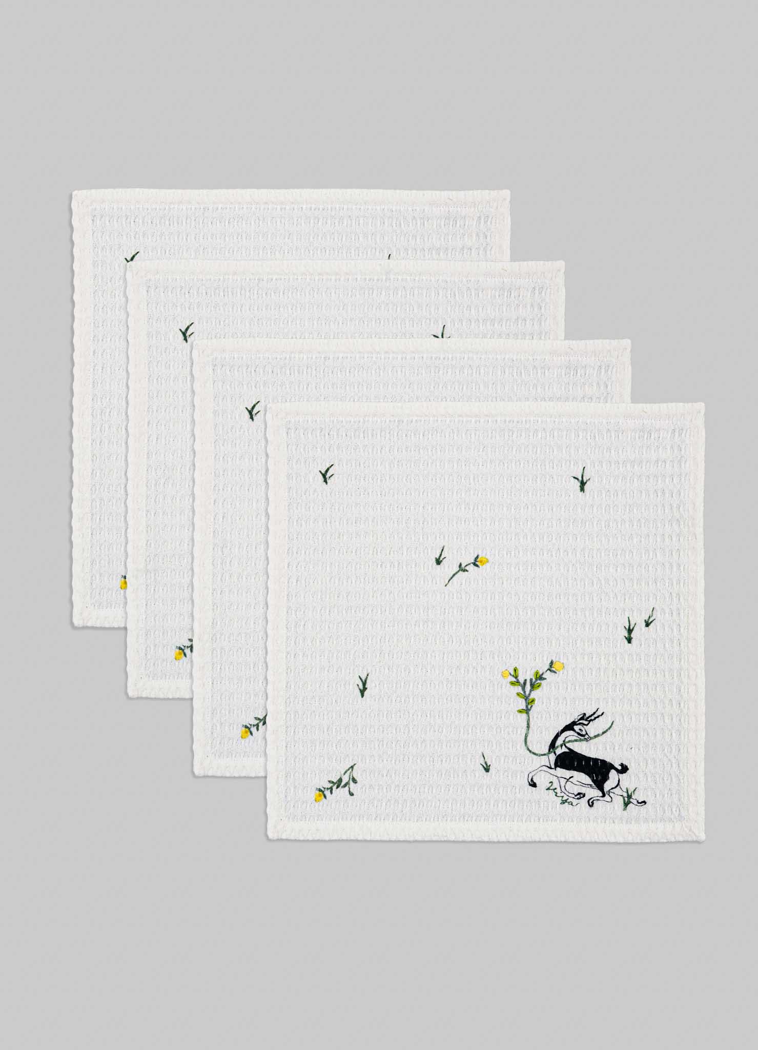 Set of four white kitchen towels with embroidered floral and animal motifs in yellow and green, featuring a textured waffle weave pattern.
