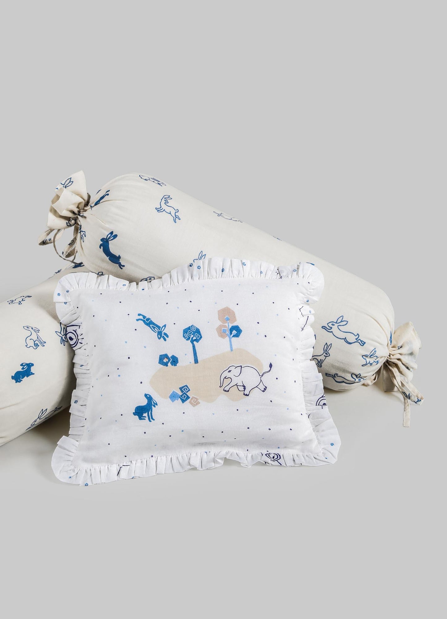 Decorative textile set including a rectangular cushion and two bolster pillows, made of soft fabric with animal and nature motifs in shades of blue and beige, featuring ruffled edges and tied ends on the bolster pillows.