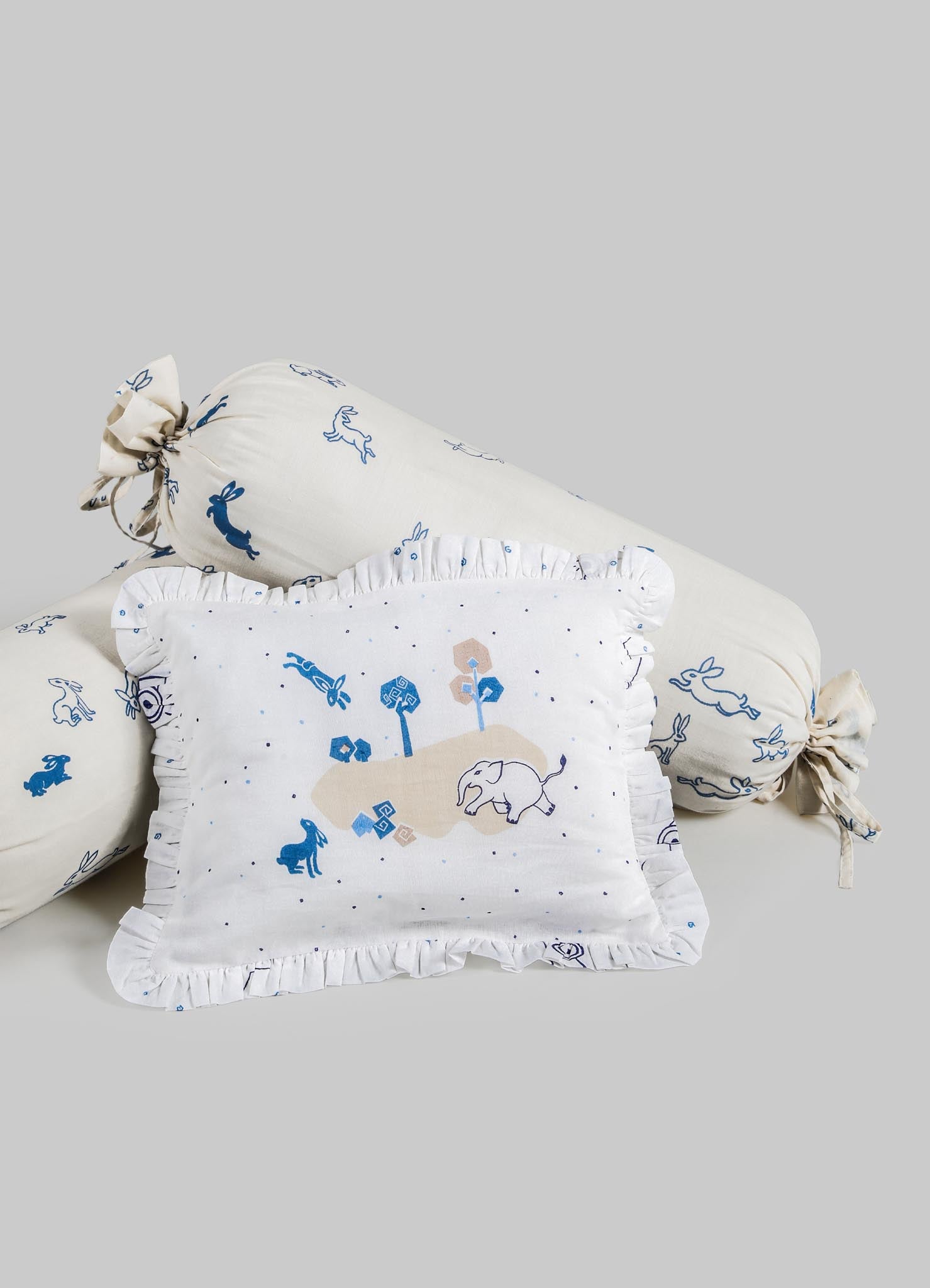 Decorative textile set including a rectangular cushion and two bolster pillows, made of soft fabric with animal and nature motifs in shades of blue and beige, featuring ruffled edges and tied ends on the bolster pillows.