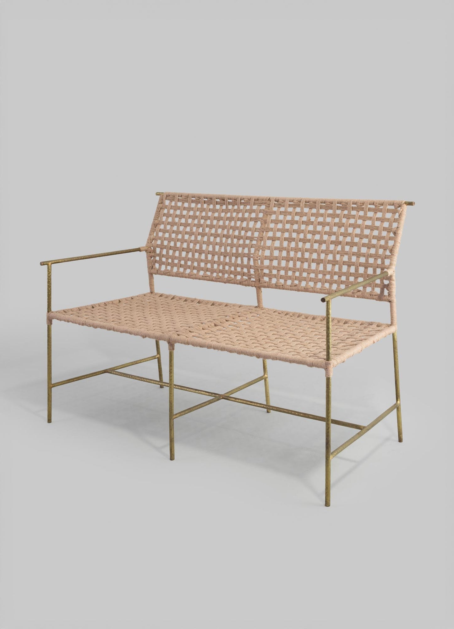 A vintage-style bench with a metal frame finished in aged brass and a woven rattan seat and backrest, showcasing a rustic, handcrafted appearance. The design features a geometric, grid-like pattern in the rattan upholstery.