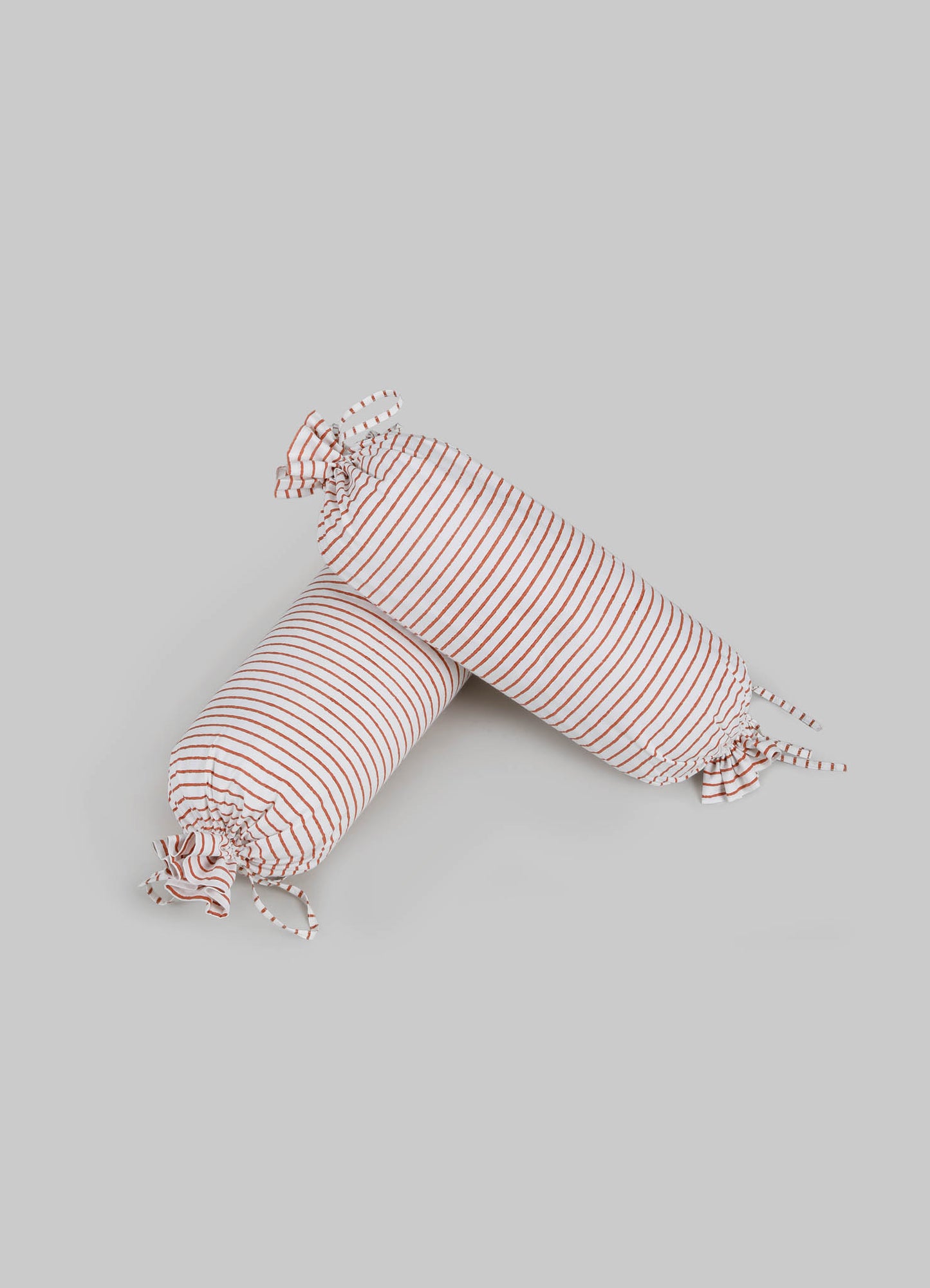 Striped fabric bolsters with ruffled ends in white and rust-colored lines, made from soft textile material.