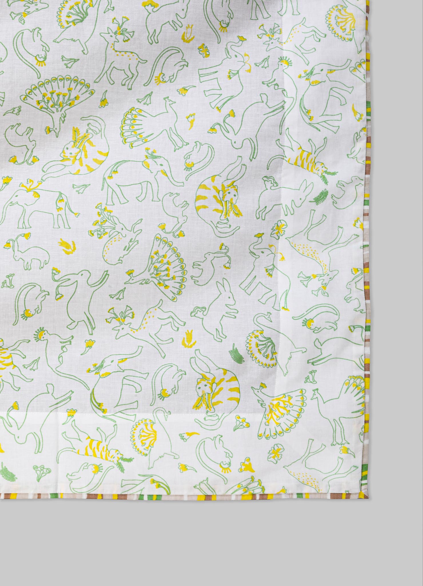 Cotton tablecloth with a playful animal-themed pattern featuring outlined elephants, lions, and rabbits in green and yellow. The fabric has a natural white background with a multicolored striped border.