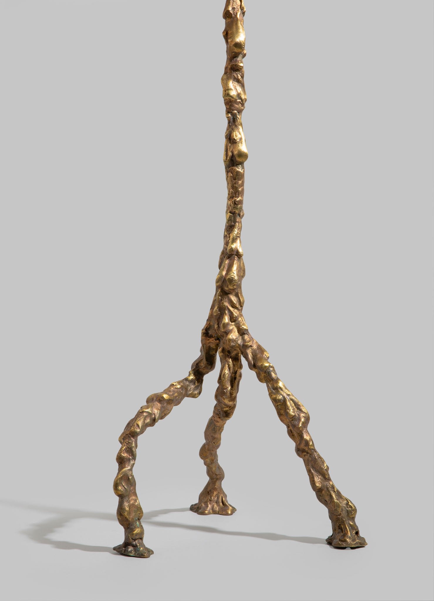 A sculptural table lamp base crafted from textured, organic-shaped brass with a metallic gold finish, featuring a tripod-like structure with three uneven, organic legs.