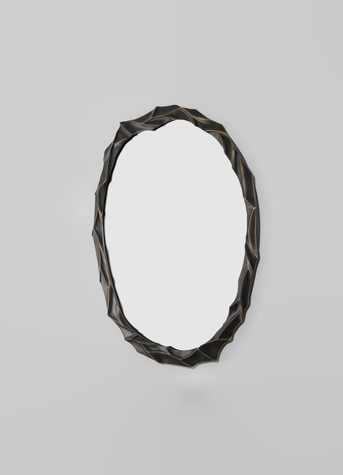 Decorative oval mirror with a textured, wavy black frame accented with subtle gold lines, mounted on a light gray wall.