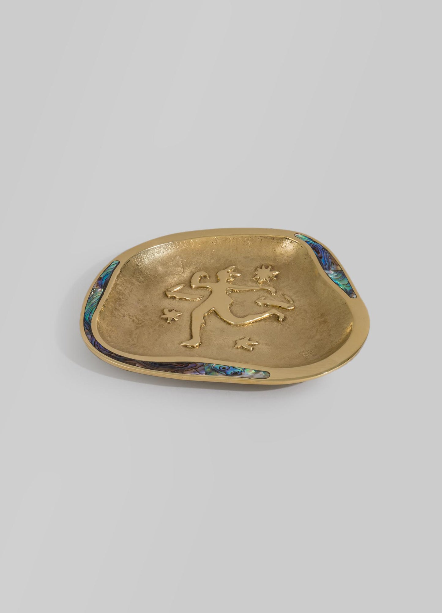 A gold-toned metal dish with an engraved lion motif in the center and iridescent abalone shell inlays along the rim. The dish has a smooth, rounded, irregular shape with a decorative and artistic appearance.