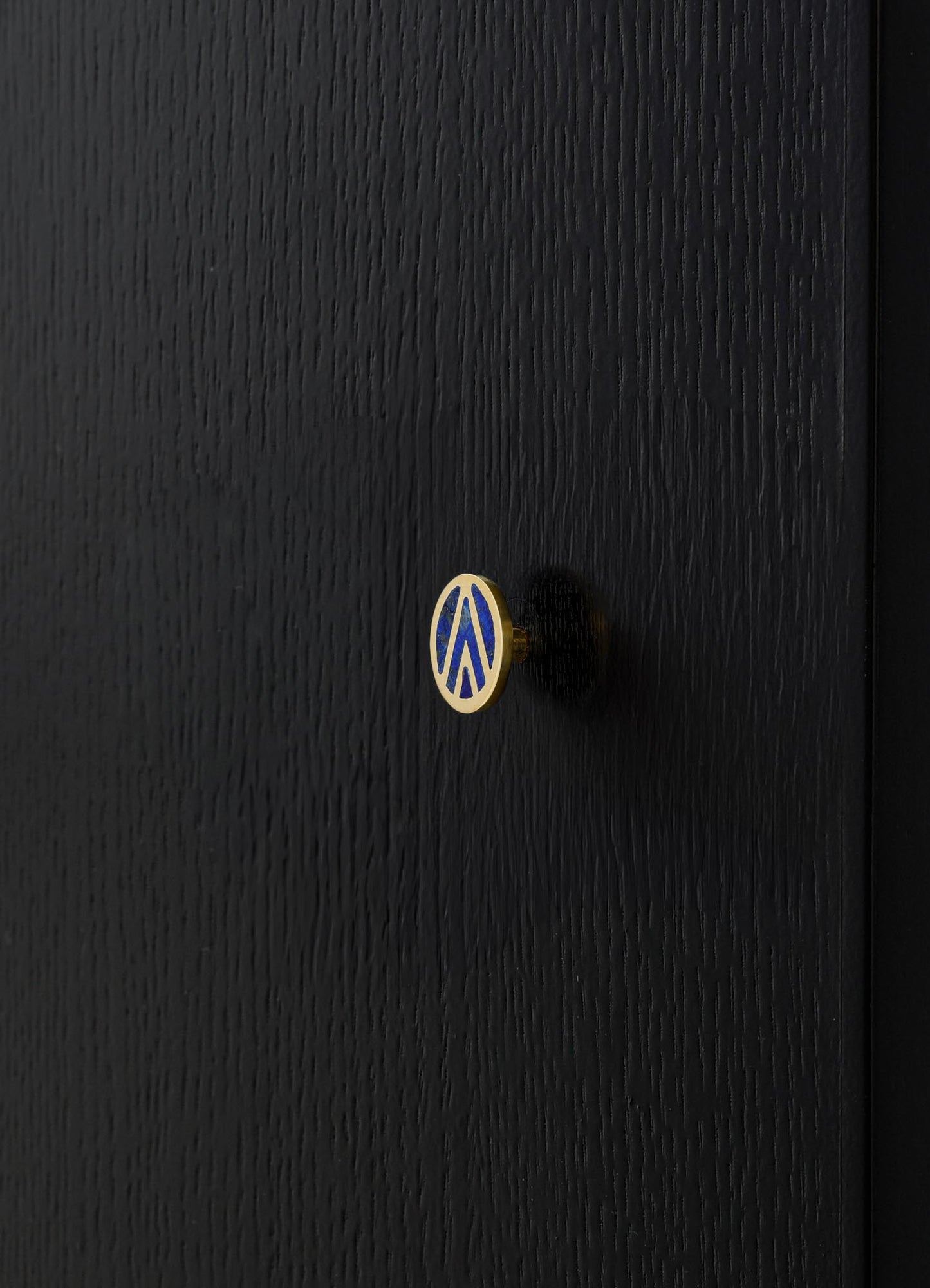 A black wooden cabinet with a textured finish, featuring a small round knob with a blue and gold geometric pattern motif. The style appears modern and minimalist.