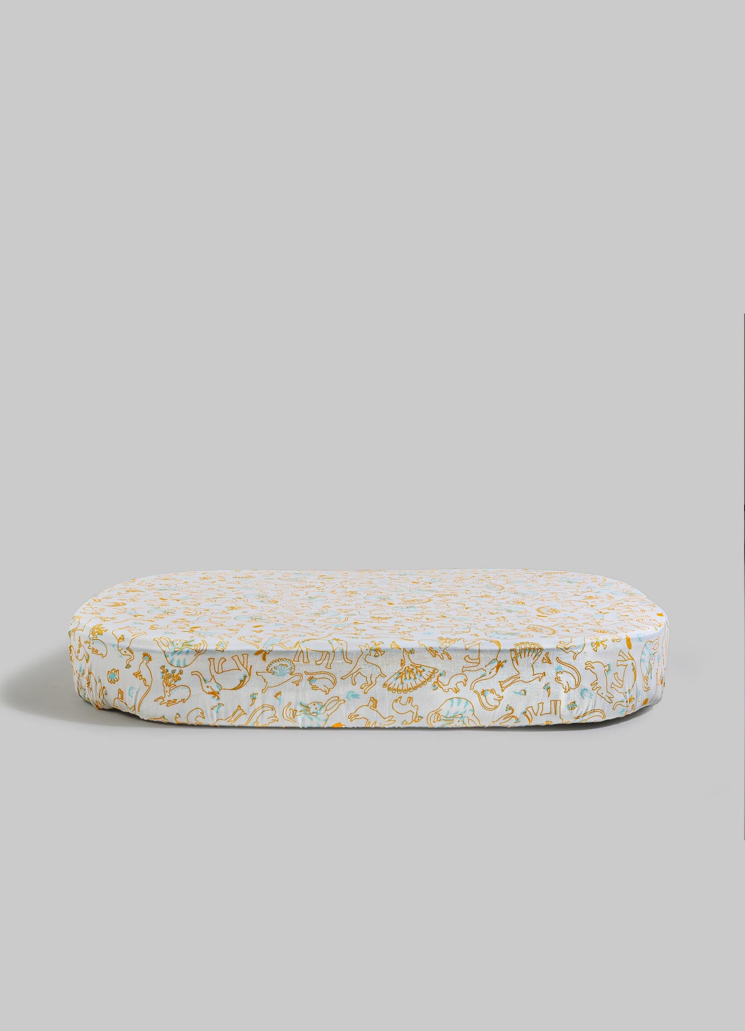 A cushioned floor mat with a white background and a pattern of animals and floral motifs in gold, light blue, and orange tones, shaped in an elongated oval form.