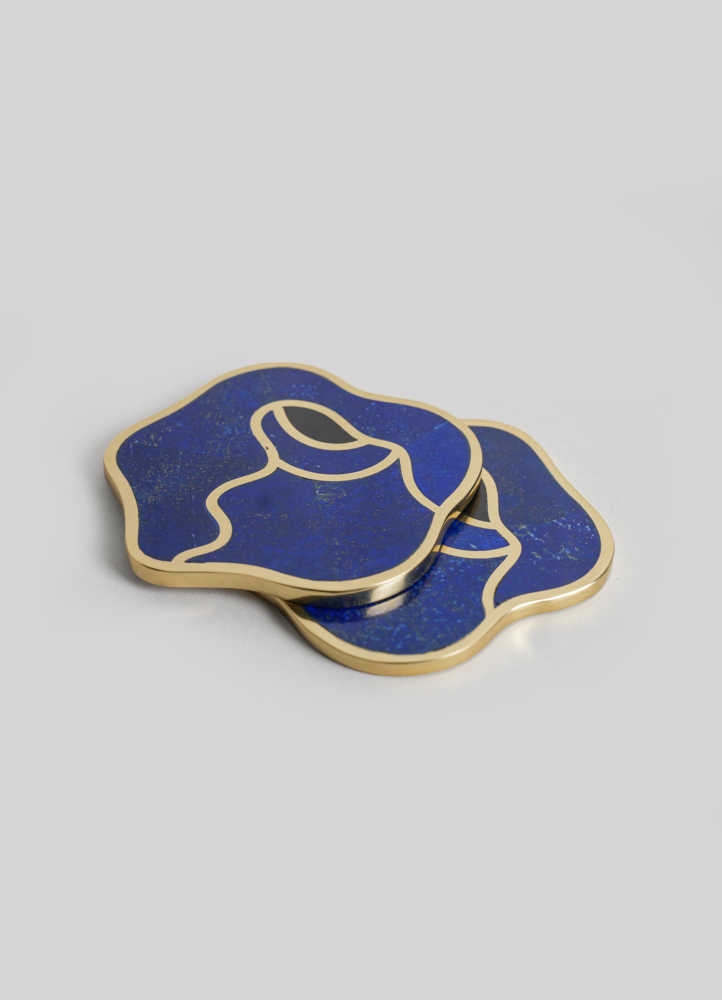 Pair of abstract coasters with dark blue, gold-speckled pattern and gold metal edges, featuring a fluid, outline-style design on a neutral background.