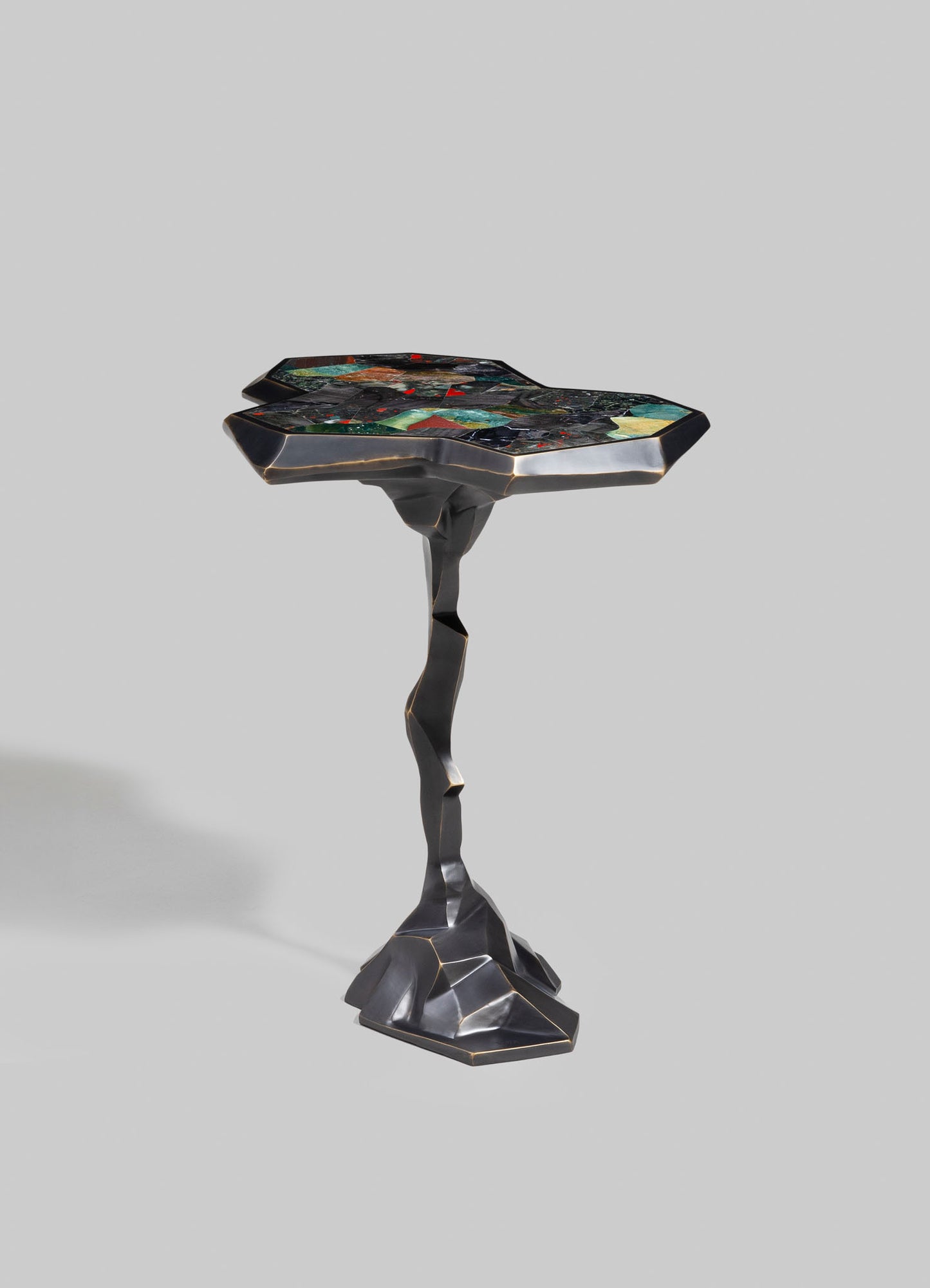 A sculptural side table with a distinctive, irregular-shaped top featuring multicolored inlay and a polished, dark metallic finish. The table has an artistically twisted, organic-shaped base with a sleek, modern look.