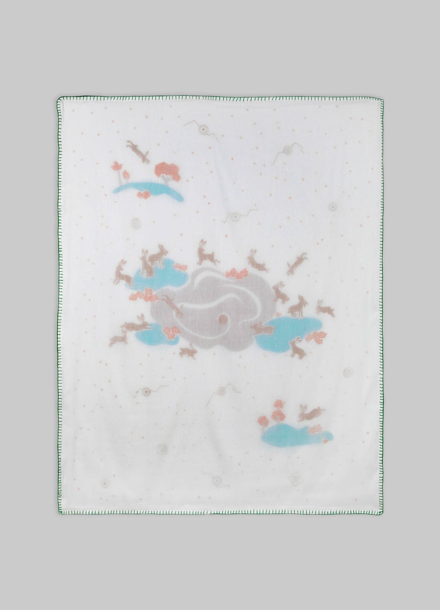 The image features a printed cotton or fabric cloth with a pattern of clouds, animals, and small abstract shapes in pastel blue, pink, and beige tones, with a green stitched border.