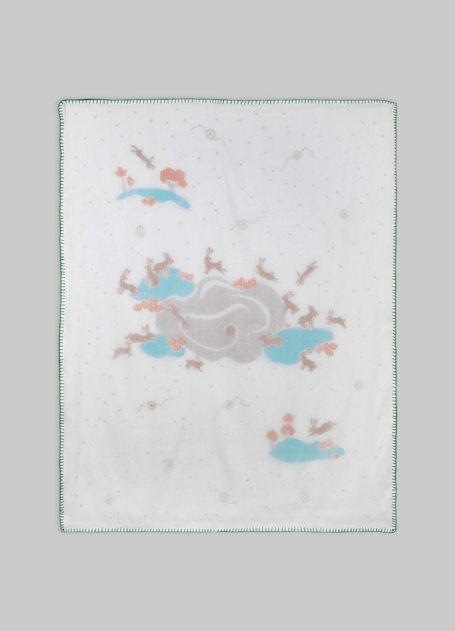 The image features a printed cotton or fabric cloth with a pattern of clouds, animals, and small abstract shapes in pastel blue, pink, and beige tones, with a green stitched border.