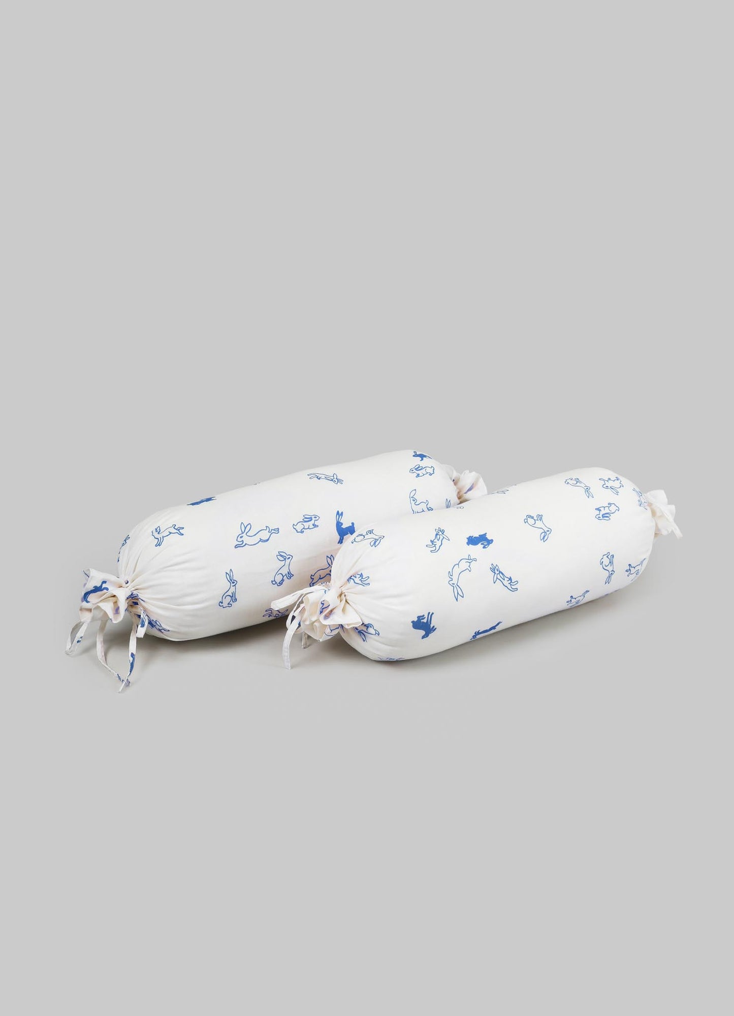Two cylindrical bolster cushions with white fabric covers featuring blue animal and bunny patterns, tied at both ends with matching fabric bows.