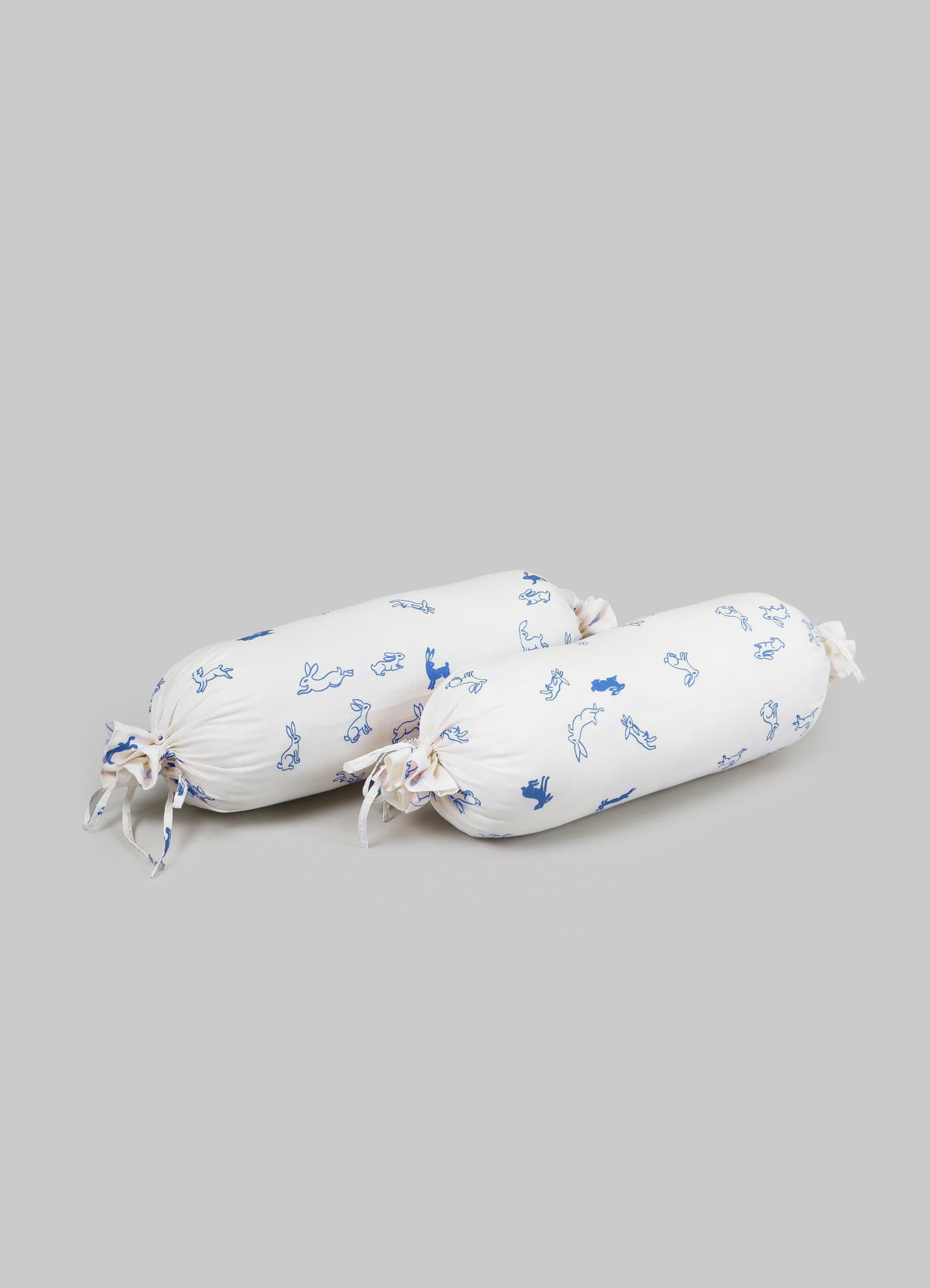 Two cylindrical bolster cushions with white fabric covers featuring blue animal and bunny patterns, tied at both ends with matching fabric bows.