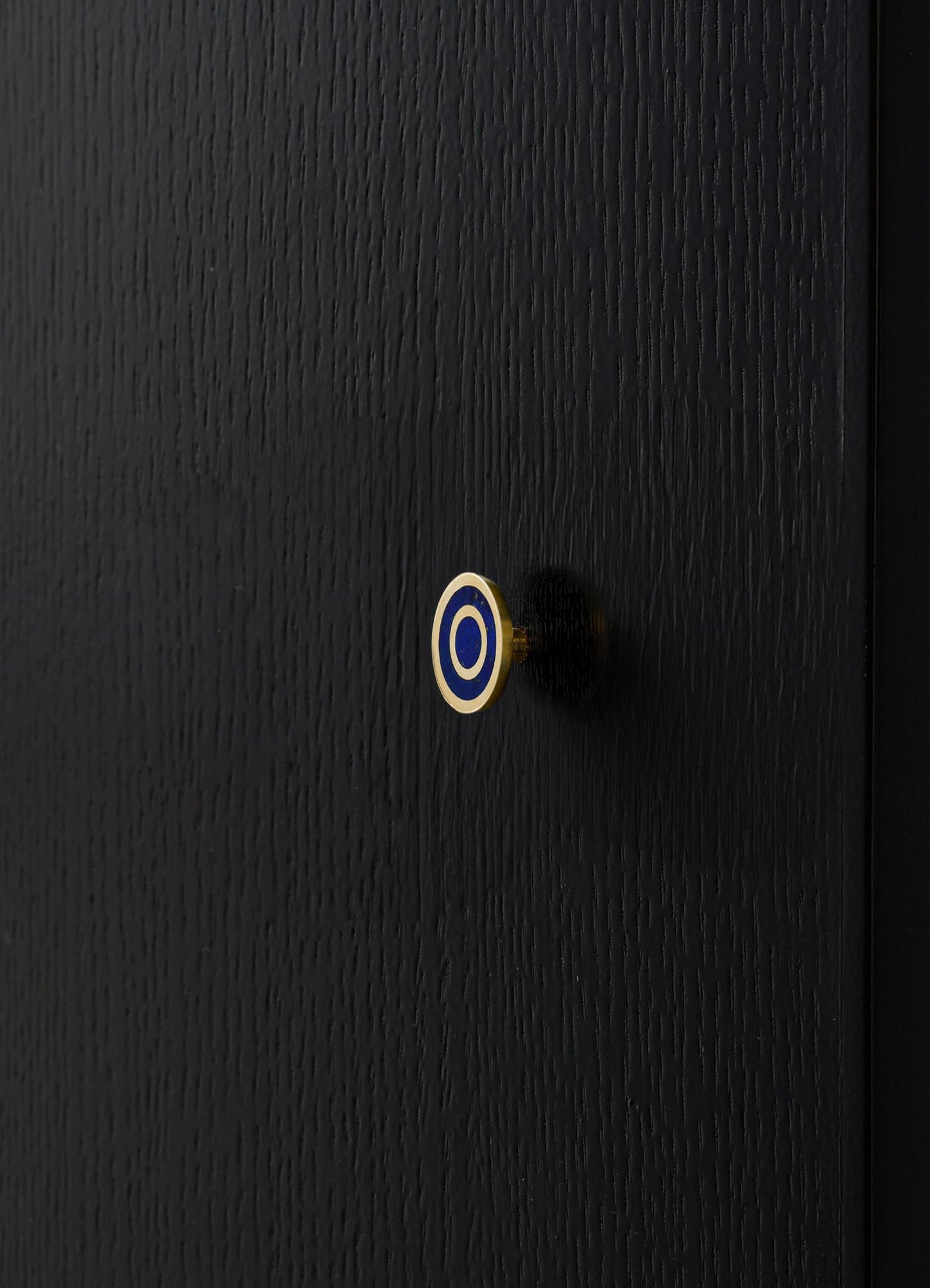 A black wooden surface with a textured finish, featuring a small round knob with a blue and white concentric circle motif.