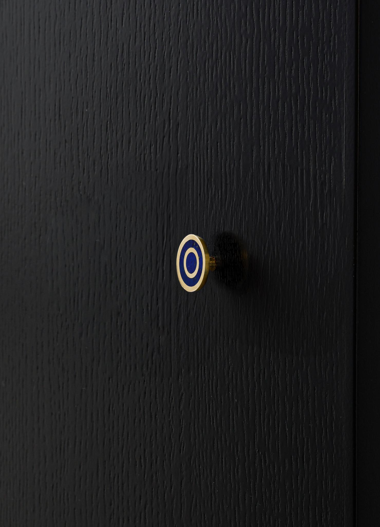 A black wooden surface with a textured finish, featuring a small round knob with a blue and white concentric circle motif.