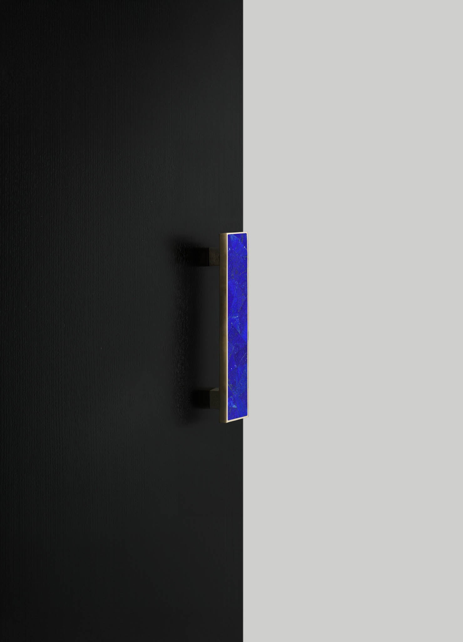 A contemporary wall-mounted light fixture with a rectangular blue glass shade and a metallic finish, installed on a black wall. The design features clean lines and a minimalist aesthetic.