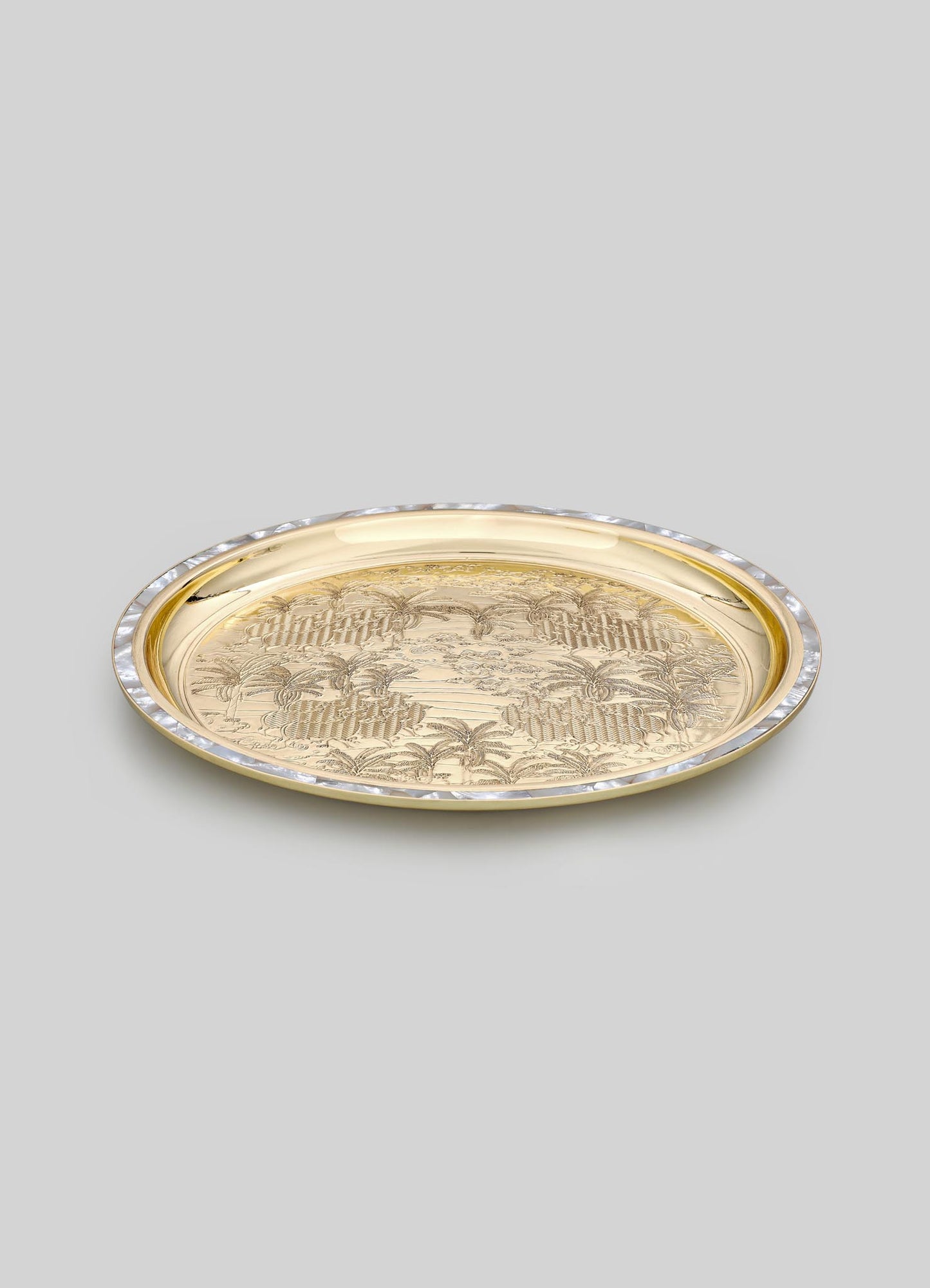 A polished gold tray with engraved palm tree and landscape motifs, featuring a decorative edge with iridescent accents, presented on a neutral background.
