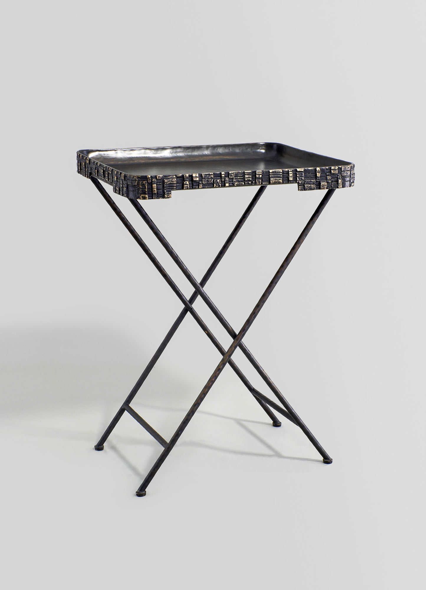 A black metal side table with a rectangular tray top featuring a textured, geometric pattern around the edges. The table has a minimalist, contemporary design with slender, intersecting legs forming an X-shape.