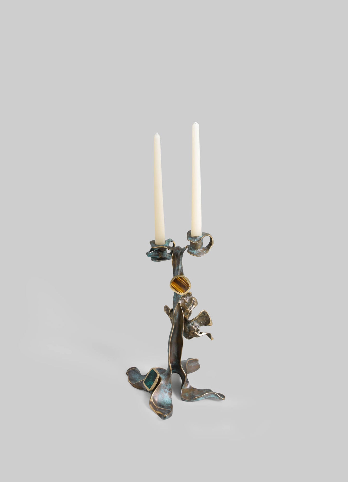 A metal candle holder with an abstract, organic design featuring a bronze finish and multiple branching arms, holding two white taper candles.