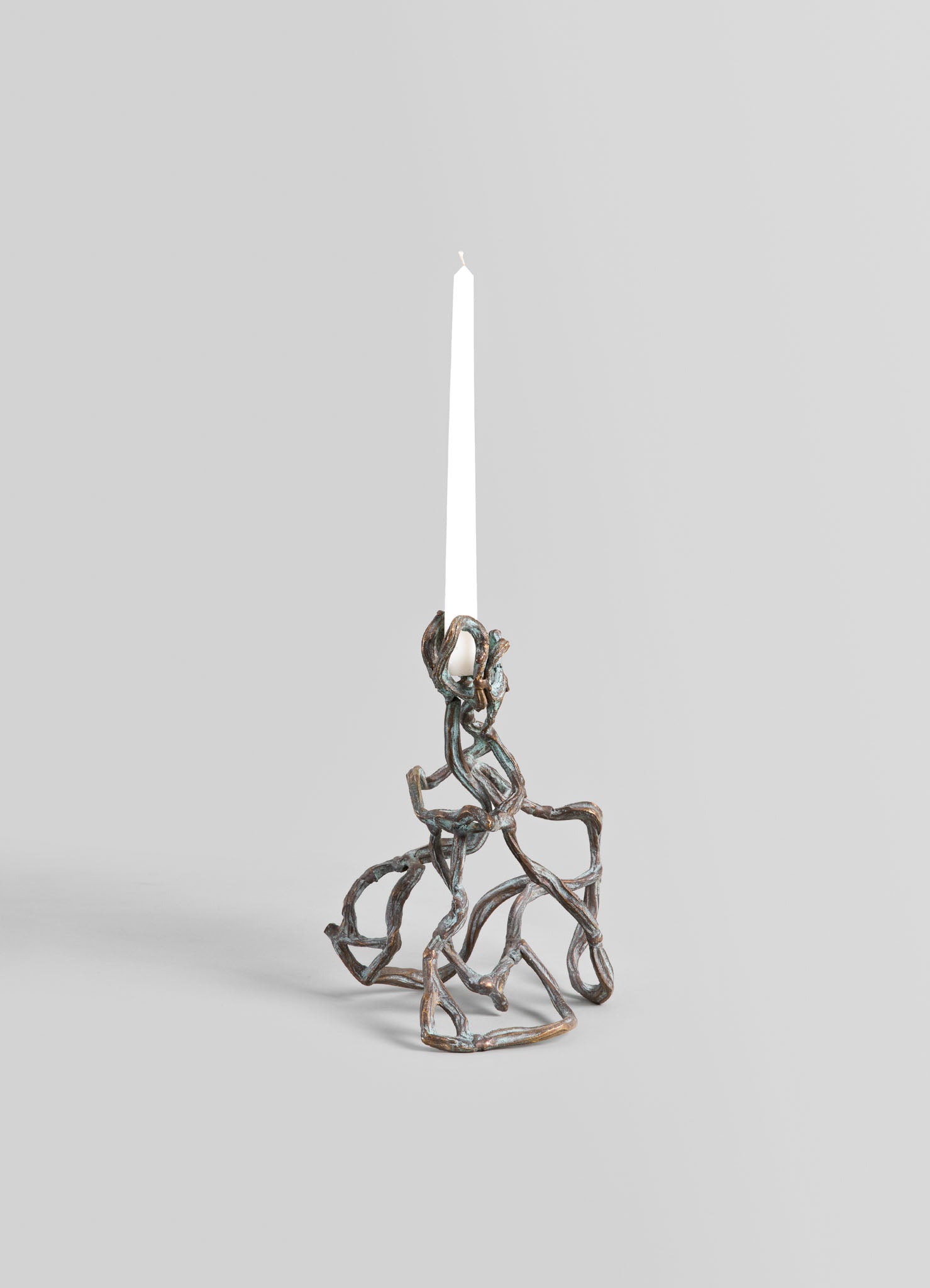 A decorative candle holder with an organic, branch-like design in a metallic bronze finish, holding a tall white taper candle. The piece has a handcrafted, rustic style with natural, flowing motifs.