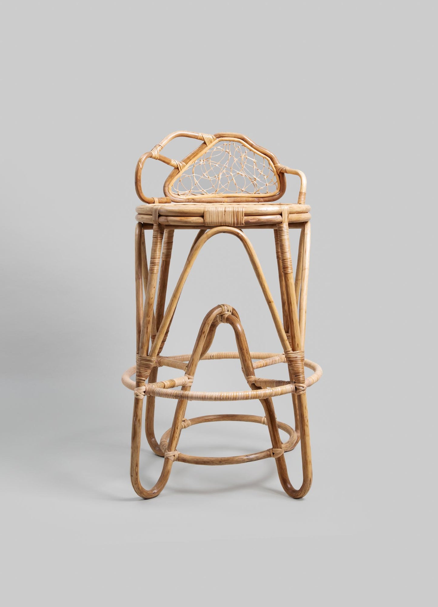 Stacked rattan stools with curved, natural finish and openwork backrests in a rustic, handcrafted style.
