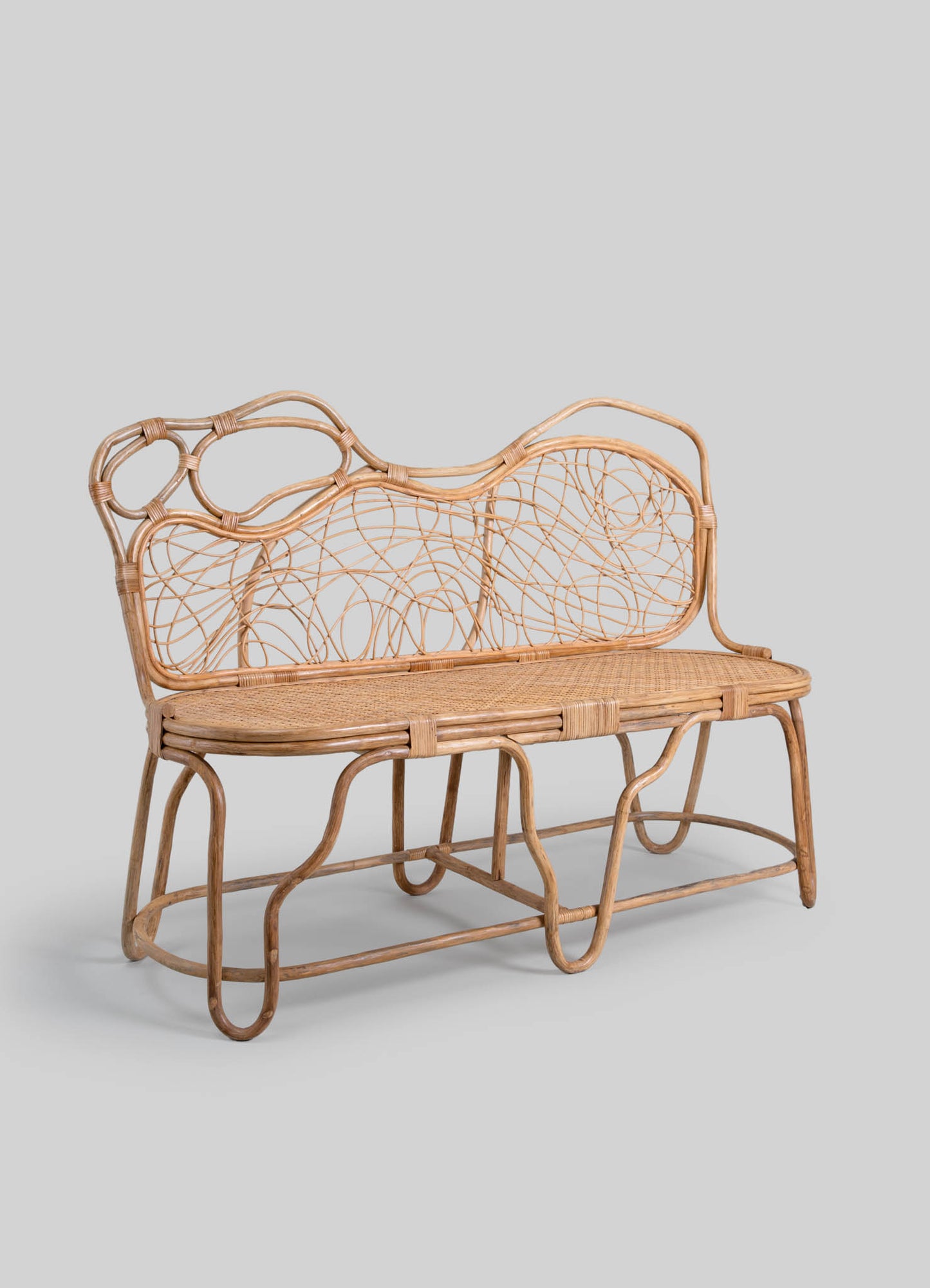 Rattan bench with a curved silhouette, featuring a woven seat and an intricate backrest with intersecting circular and linear patterns, set against a neutral background.