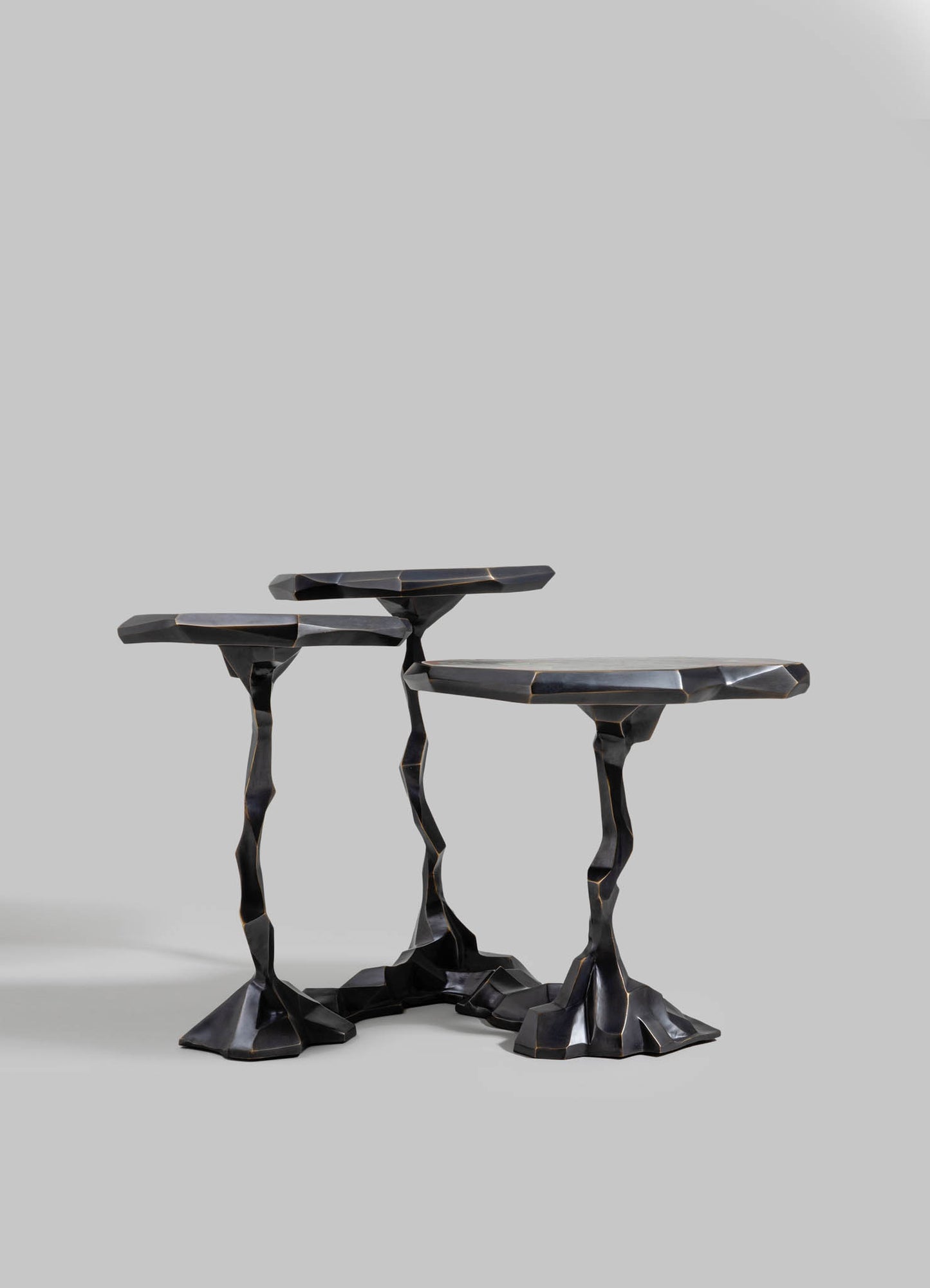 Black sculptural side tables with irregular, sculpted legs and angular tops, crafted from a dark, glossy material resembling wood or resin, set against a plain gray background.