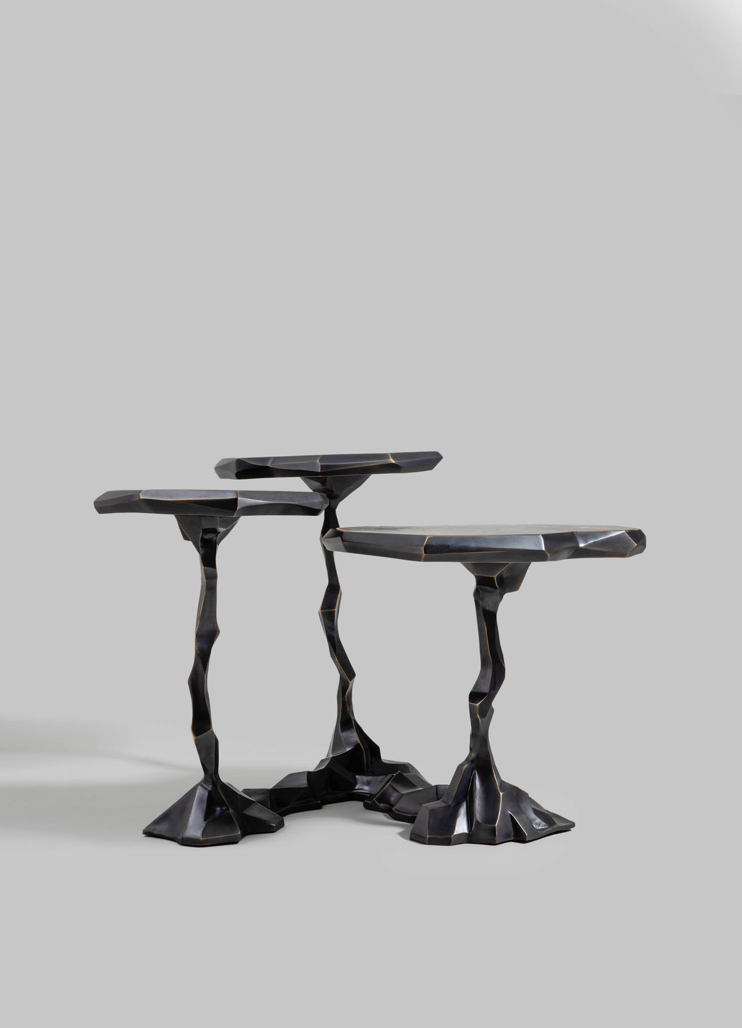 Black sculptural side tables with irregular, sculpted legs and angular tops, crafted from a dark, glossy material resembling wood or resin, set against a plain gray background.