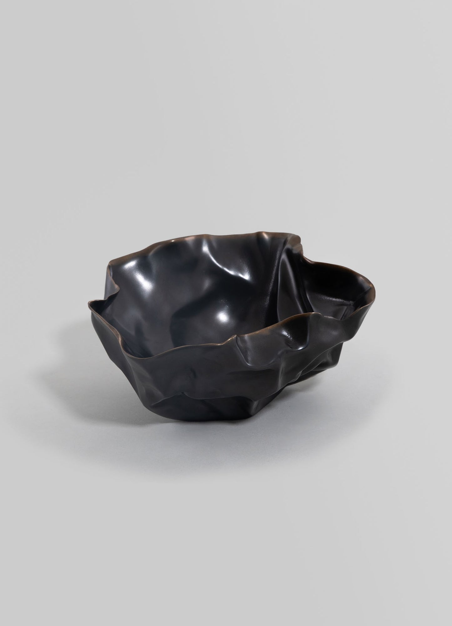 A black ceramic bowl with an irregular, wavy edge and a glossy finish, featuring a handcrafted, organic shape.
