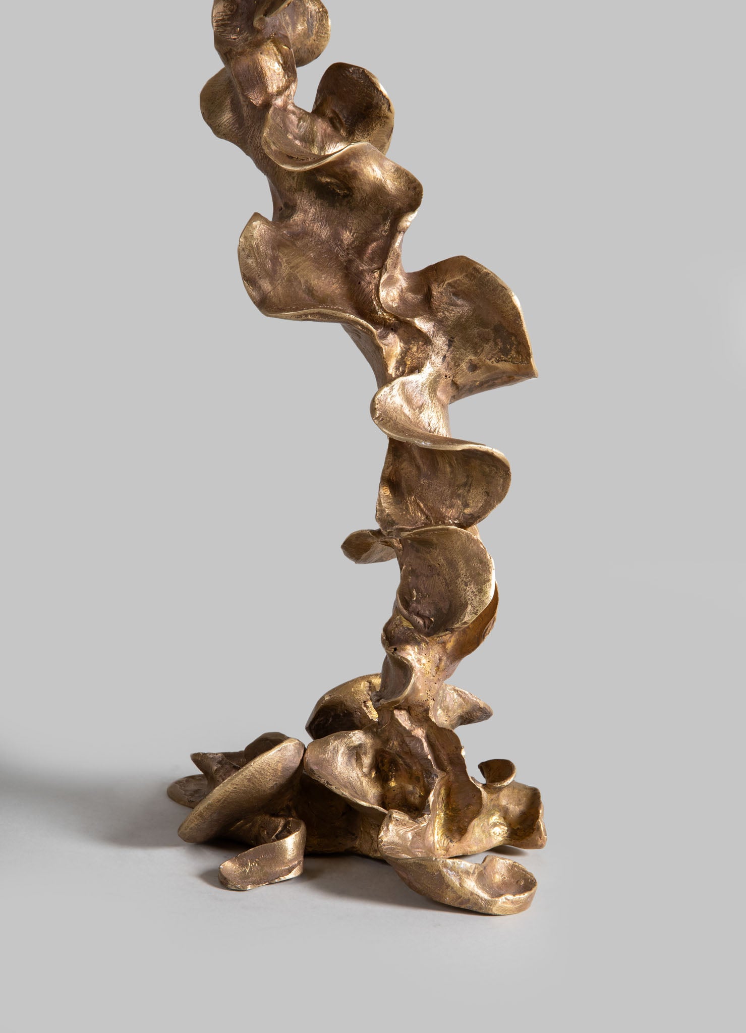A sculptural decorative piece crafted from metal with a polished bronze finish, featuring abstract, organic shapes resembling flowing, folded forms. The sculpture has a contemporary style with smooth, undulating surfaces.