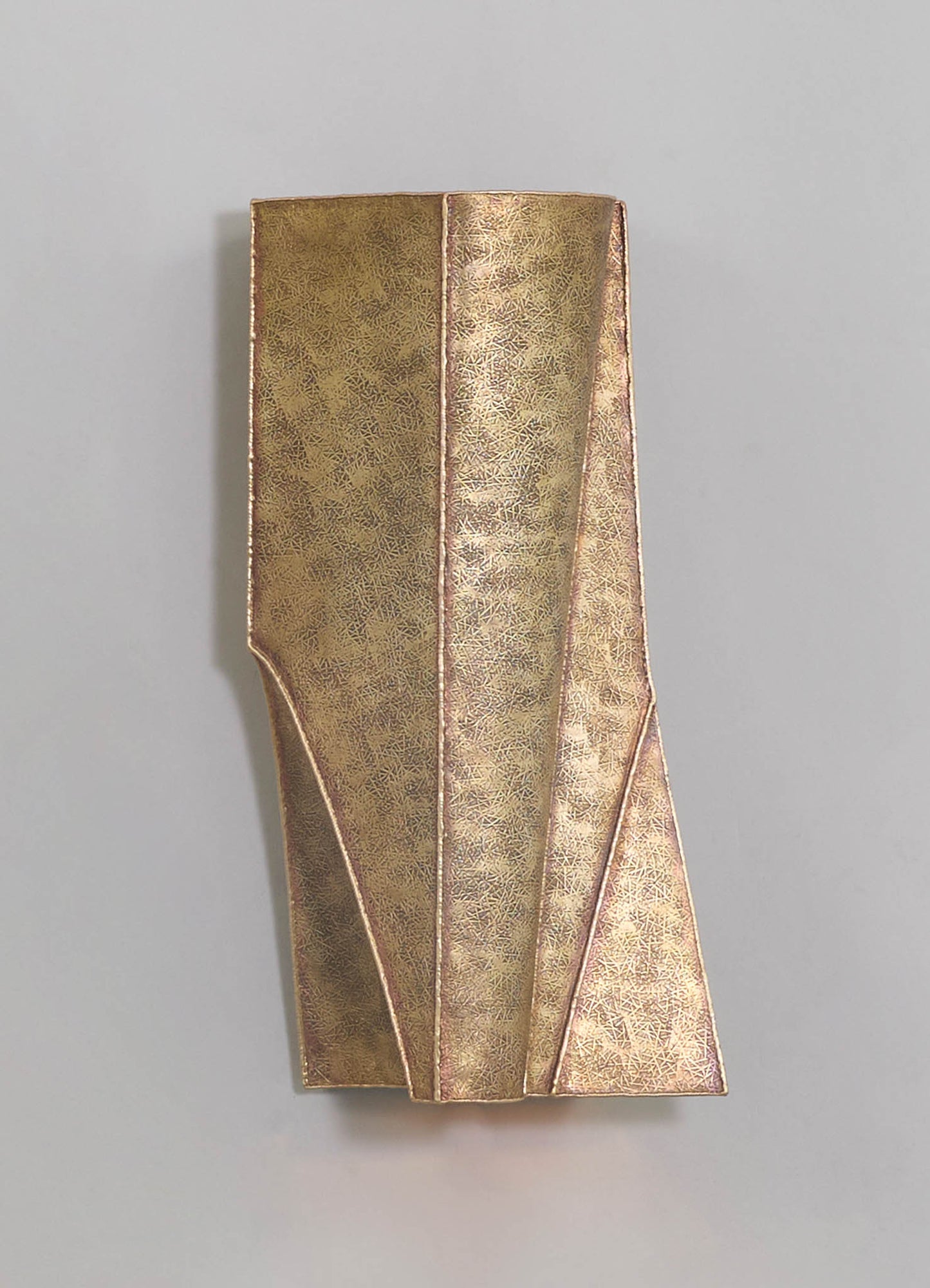A decorative gold-colored metal vase with a textured surface featuring geometric patterning and angular lines, set against a neutral background.
