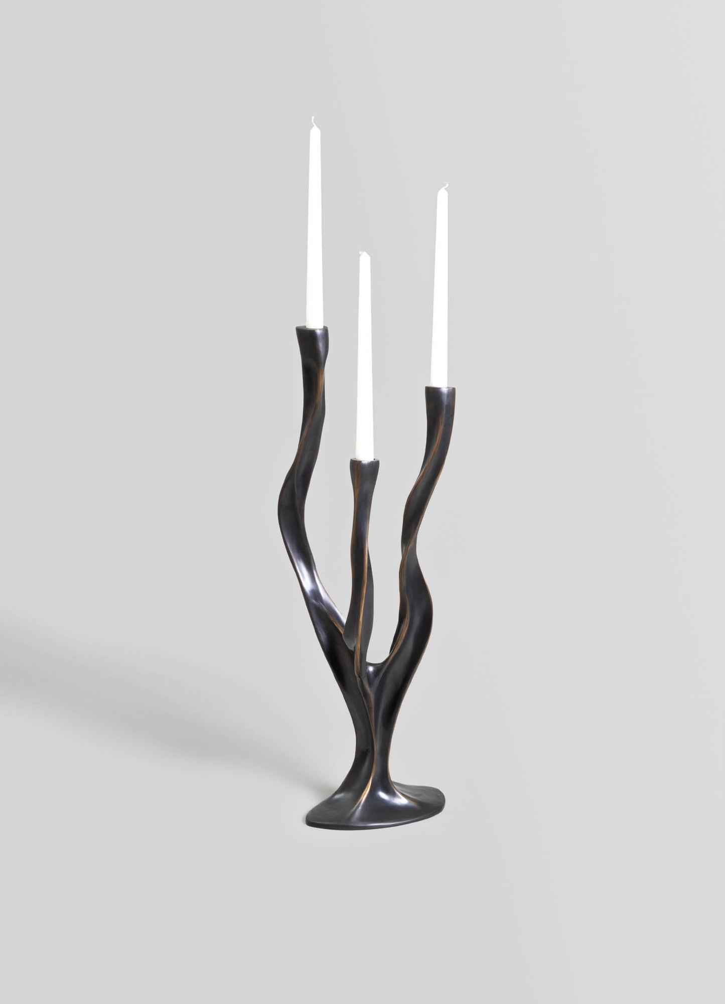 Metallic sculpture with a twisting, organic form, finished in a dark, polished surface, designed as a decorative piece for contemporary interiors. The sculpture features three slender, tapering candle holders with white candles.