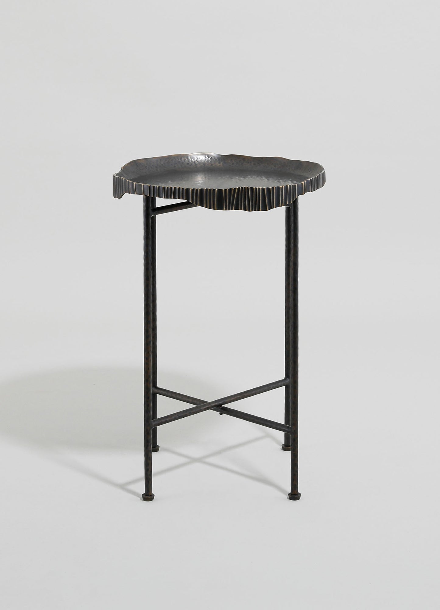 A metal side table with an irregularly shaped, textured dark surface resembling a leaf or organic form, supported by slender, straight metal legs. The table has a contemporary style with a matte dark finish.